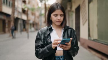 Young hispanic woman with winner expression using smartphone at street