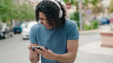 Genç Latin adam gülümsüyor. Sokakta akıllı telefondan video seyrediyor.