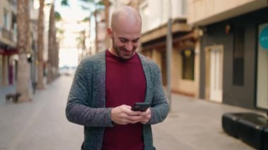 Sokakta akıllı telefon kullanarak kendine güvenen genç kel adam.