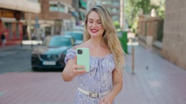 Young blonde woman using smartphone with cheerful expression at street