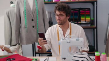 Young hispanic man tailor smiling confident having video call at clothing factory