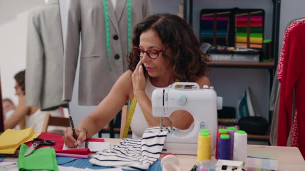 服装厂中年女性裁缝在笔记本上讲智能手机 — 图库视频影像