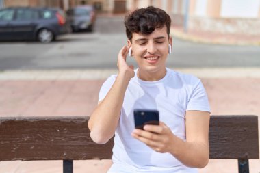 Non binary man listening to music sitting on bench at park