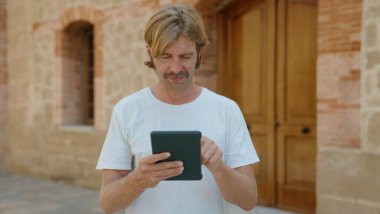 Sarışın genç adam sokakta ciddi bir ifadeyle dokunmatik ped kullanıyor.