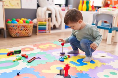 Adorable hispanic boy playing with hoops toys standing at kindergarten
