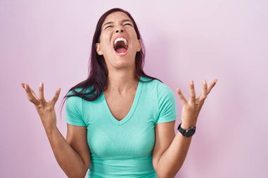 Pembe arka planda duran genç İspanyol kadın kızgın ve deli gibi bağırıyor ve agresif bir ifade ve kollarla bağırıyor. hüsran kavramı. 