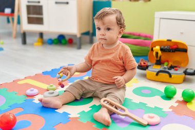 Anaokulunda yerde oturmuş oyuncaklarla oynayan sevimli sarışın çocuk.