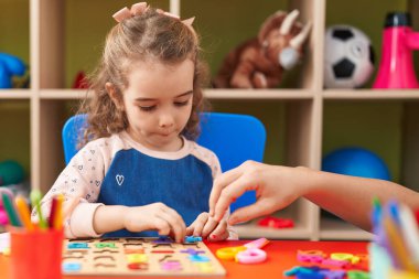 Adorable blonde girl playing with maths puzzle game sitting on table at kindergarten