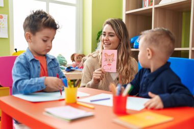Teacher with boys sitting on table having language lesson at kindergarten