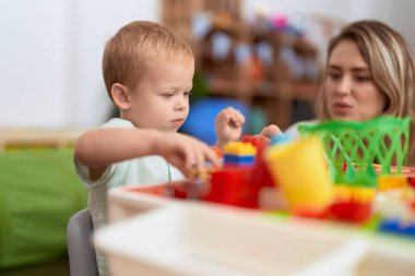 Teacher and toddler playing with construction blocks sitting on table at kindergarten
