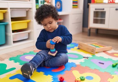 Anaokulunda yerde oturmuş halkalarla oynayan sevimli İspanyol çocuk.