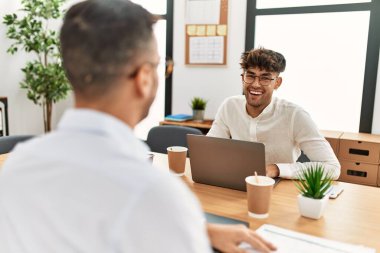 İki İspanyol iş adamı ofiste çalışırken gülümsüyor.