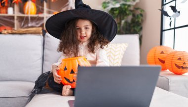 Adorable hispanic girl wearing halloween costume using laptop at home