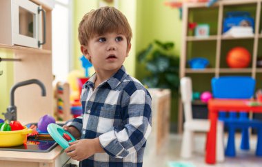 Adorable hispanic boy playing with play kitchen standing at kindergarten