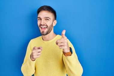 Hispanic man standing over blue background pointing fingers to camera with happy and funny face. good energy and vibes. 