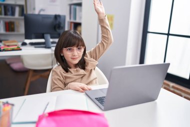 Adorable hispanic girl student having lesson with hand raised up at classroom