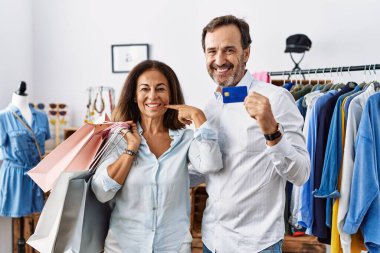 Hispanic middle age couple holding shopping bags and credit card smiling cheerful showing and pointing with fingers teeth and mouth. dental health concept. 