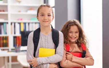 Two kids students wearing backpack holding book at classroom