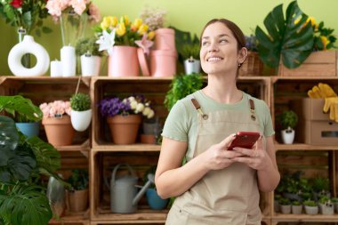 Young beautiful woman florist smiling confident using smartphone at flower shop