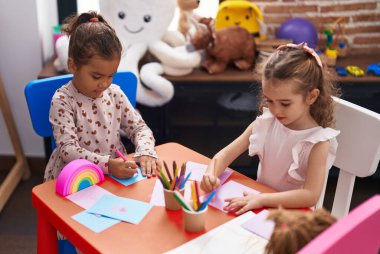 Two kids preschool students sitting on table drawing on paper at kindergarten