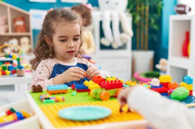 Adorable blonde girl playing with construction blocks sitting on table at kindergarten