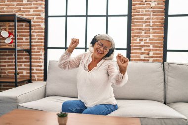 Orta yaşlı bir kadın evdeki kanepede oturmuş müzik dinliyor.