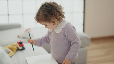 Adorable hispanic girl drawing on notebook standing at home