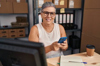 Middle age woman ecommerce business worker using smartphone at office