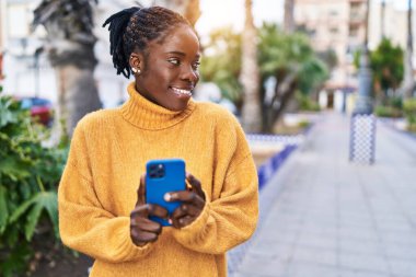 Afro-Amerikalı kadın sokakta akıllı telefon kullanarak kendine güveniyor.