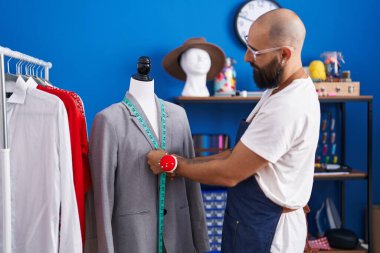 Young bald man tailor measuring jacket at clothing factory