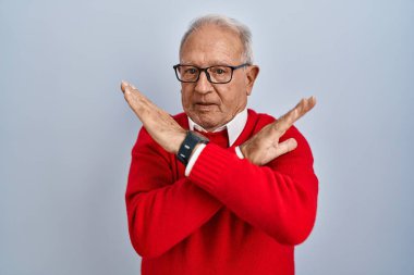 Senior man with grey hair standing over isolated background rejection expression crossing arms doing negative sign, angry face 
