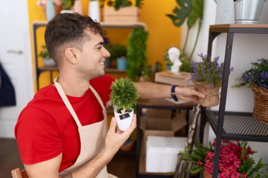Young hispanic man florist smiling confident holding plants at flower shop