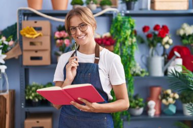 Young blonde girl florist smiling confident reading book at florist