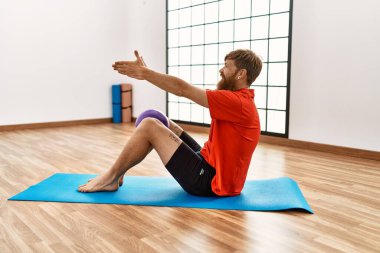 Genç kızıl saçlı, gülümseyen, kendine güvenen bir adam spor merkezinde formda top kullanıyor.