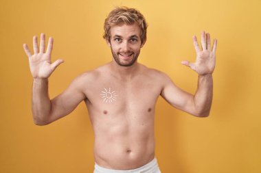 Caucasian man standing shirtless wearing sun screen showing and pointing up with fingers number ten while smiling confident and happy. 