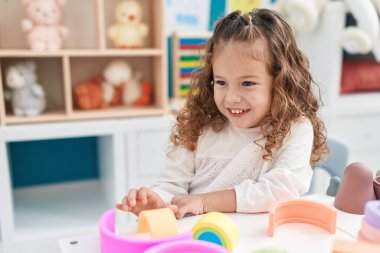 Sevimli sarışın çocuk anaokulundaki masada oyuncaklarla oynuyor.