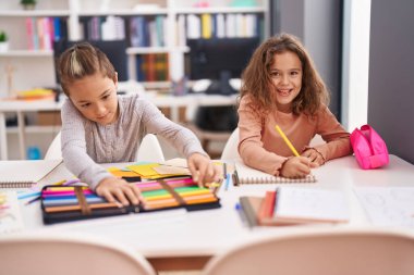 Two kids students sitting on table drawing on notebook paper at classroom