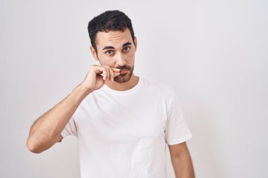 Handsome hispanic man standing over white background mouth and lips shut as zip with fingers. secret and silent, taboo talking 