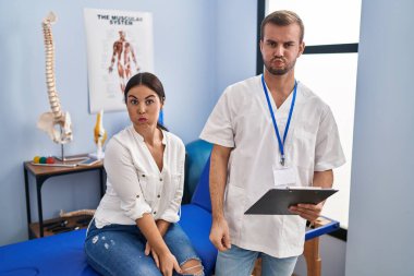 Young hispanic woman at physiotherapist appointment puffing cheeks with funny face. mouth inflated with air, crazy expression. 