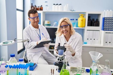 Middle age man and woman scientist partners working using microscope at laboratory