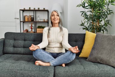 Orta yaşlı, kır saçlı, gülümseyen, yoga egzersizi yapan bir kadın.