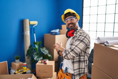 Young hispanic man with beard working at home renovation inviting to enter smiling natural with open hand 