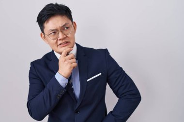 Young asian man wearing business suit and tie thinking worried about a question, concerned and nervous with hand on chin 