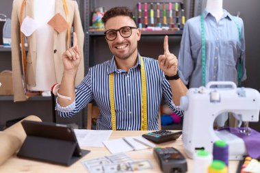 Hispanic man with beard dressmaker designer working at atelier smiling amazed and surprised and pointing up with fingers and raised arms. 