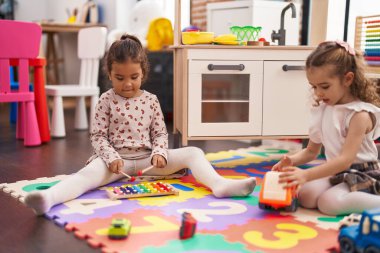 Two kids playing xylophone sitting on floor at kindergarten