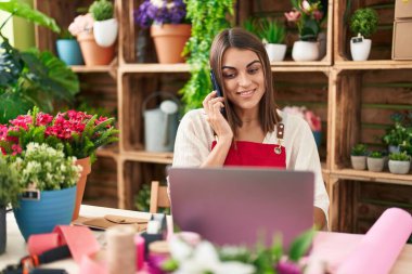 Çiçekçide dizüstü bilgisayar kullanarak konuşan güzel İspanyol çiçekçi kadın.