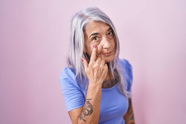 Middle age woman with tattoos standing over pink background pointing to the eye watching you gesture, suspicious expression 