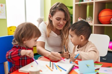 Teacher with boys sitting on table drawing on paper at kindergarten