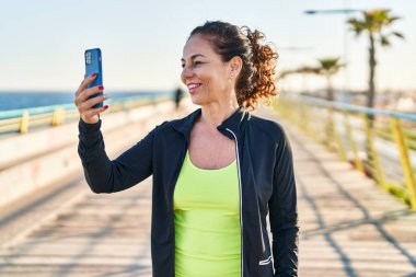 Middle age hispanic woman working out with smartphone at promenade