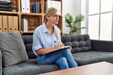 Genç sarışın psikolog, panoya yazı yazıyor klinikteki koltukta oturuyor.